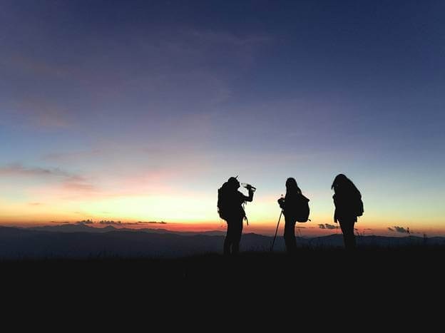 A silhouette of three hikers on a walk during sunset